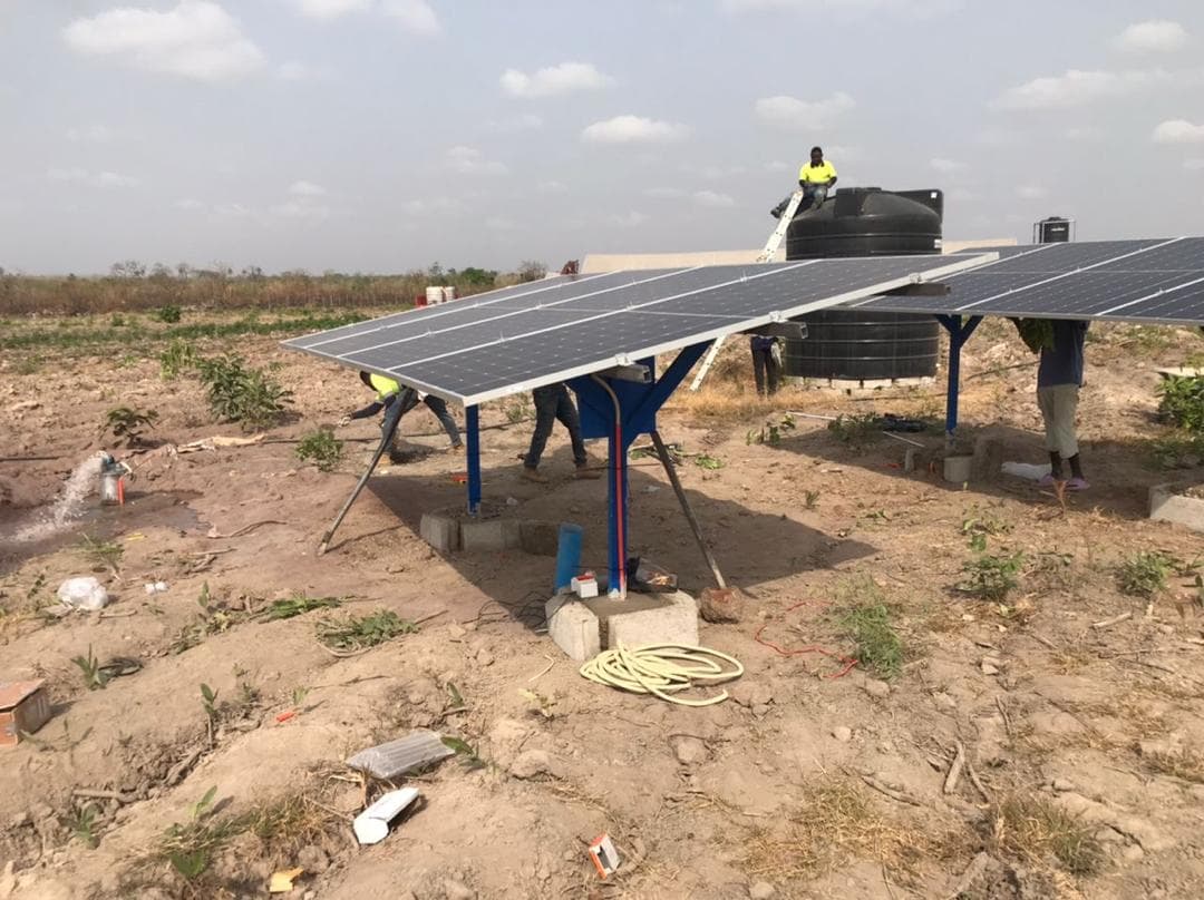 Workers commissioning a solar-powered irrigation system at Aframso farm, with water flowing from the pipe